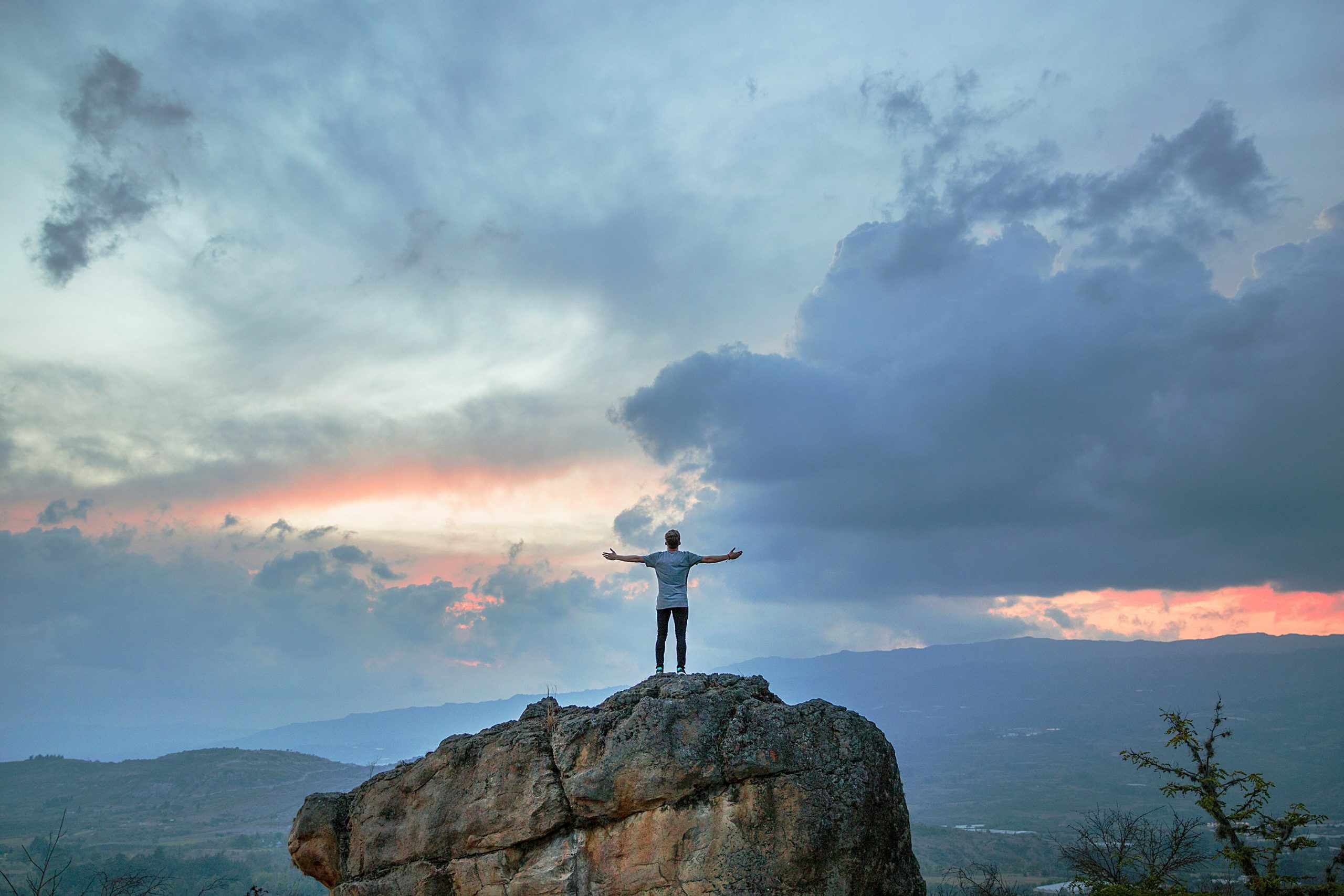 person standing with arms outstretched on mountain top